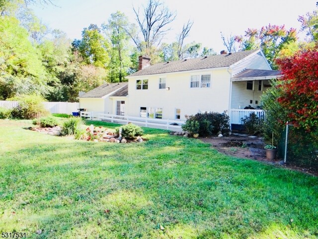 rear view of property featuring a lawn, fence, and a chimney