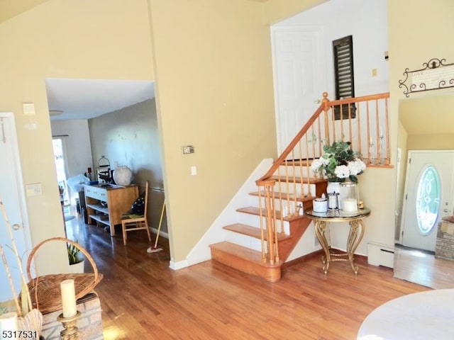 foyer with a baseboard heating unit, wood finished floors, baseboards, a towering ceiling, and stairs