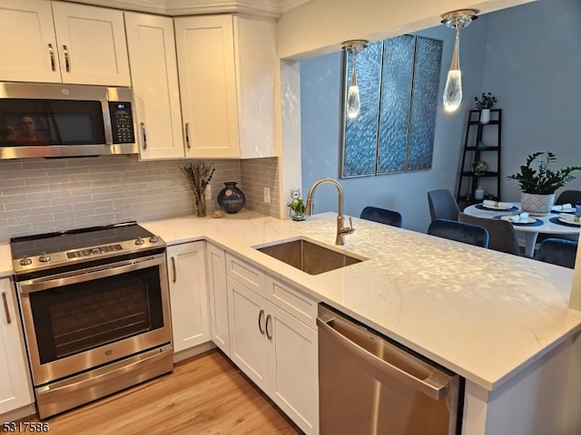 kitchen featuring sink, appliances with stainless steel finishes, decorative light fixtures, light hardwood / wood-style floors, and white cabinetry