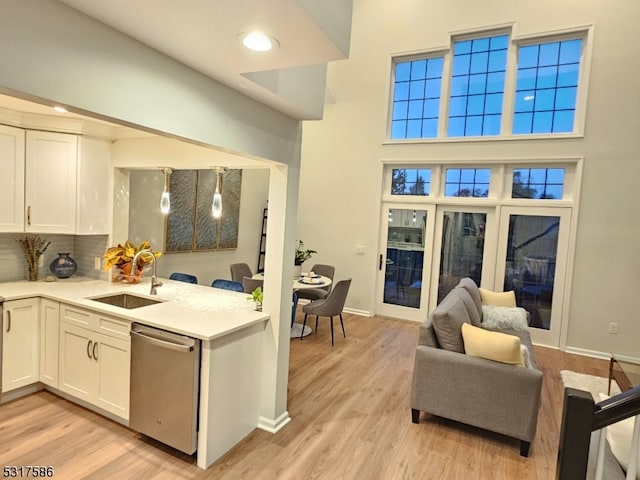 kitchen with backsplash, white cabinets, sink, stainless steel dishwasher, and light wood-type flooring