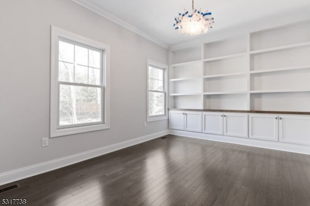 empty room featuring a healthy amount of sunlight, a notable chandelier, crown molding, and dark wood-type flooring