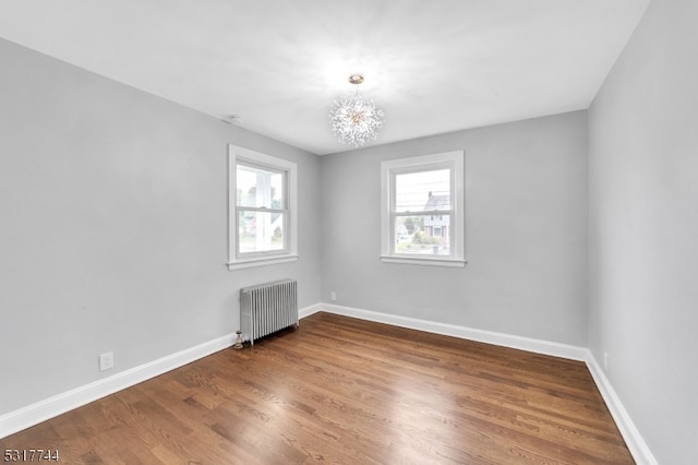 empty room with an inviting chandelier, dark hardwood / wood-style flooring, and radiator heating unit