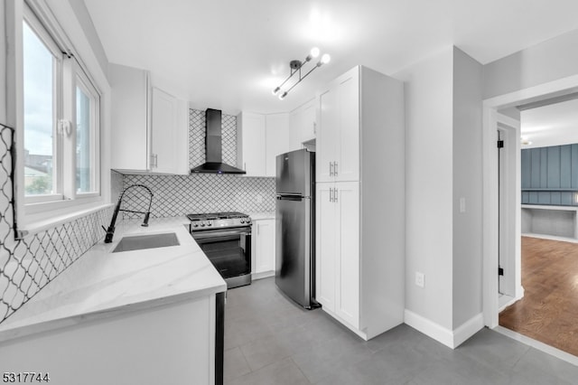 kitchen featuring light stone counters, stainless steel appliances, white cabinets, sink, and wall chimney range hood