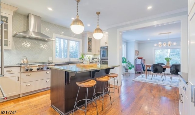 kitchen with a kitchen island, dark stone counters, white cabinets, a breakfast bar area, and wall chimney exhaust hood