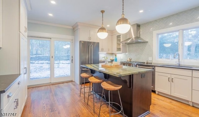 kitchen featuring sink, a center island, wall chimney range hood, stainless steel appliances, and white cabinets