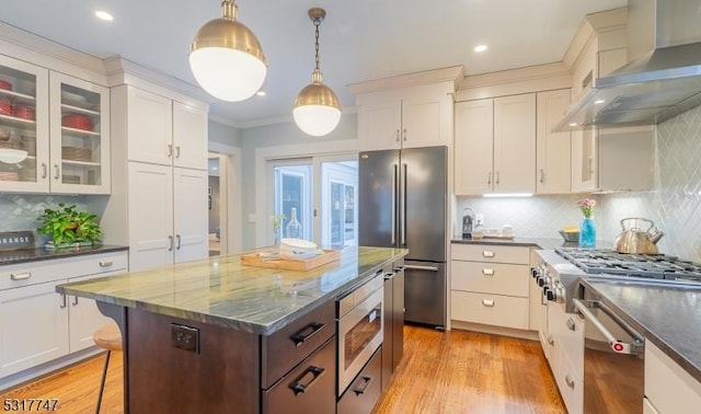 kitchen with appliances with stainless steel finishes, wall chimney range hood, decorative light fixtures, a breakfast bar, and a kitchen island