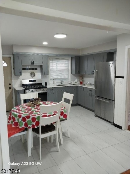 kitchen with sink, light tile patterned flooring, appliances with stainless steel finishes, gray cabinets, and backsplash