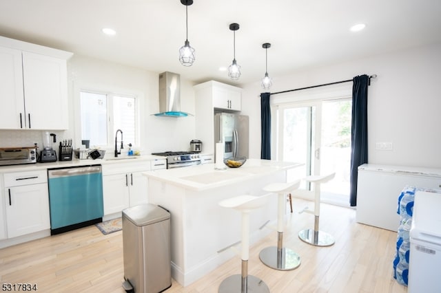 kitchen featuring appliances with stainless steel finishes, light wood-type flooring, wall chimney range hood, and white cabinetry