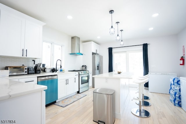 kitchen featuring wall chimney exhaust hood, a kitchen island, light hardwood / wood-style flooring, white cabinets, and appliances with stainless steel finishes