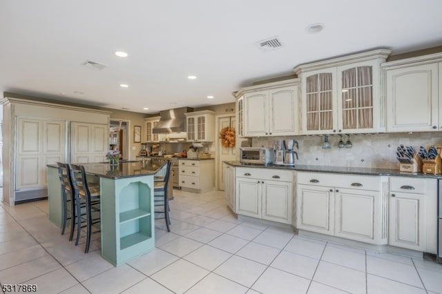 kitchen with wall chimney range hood, a center island, light tile patterned floors, and tasteful backsplash