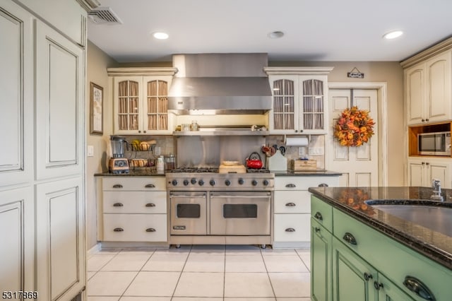 kitchen featuring green cabinets, appliances with stainless steel finishes, light tile patterned floors, and wall chimney range hood