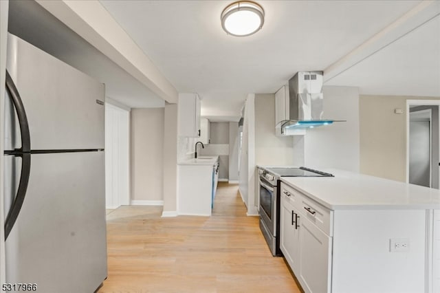 kitchen with light wood-type flooring, stainless steel appliances, sink, wall chimney range hood, and white cabinetry