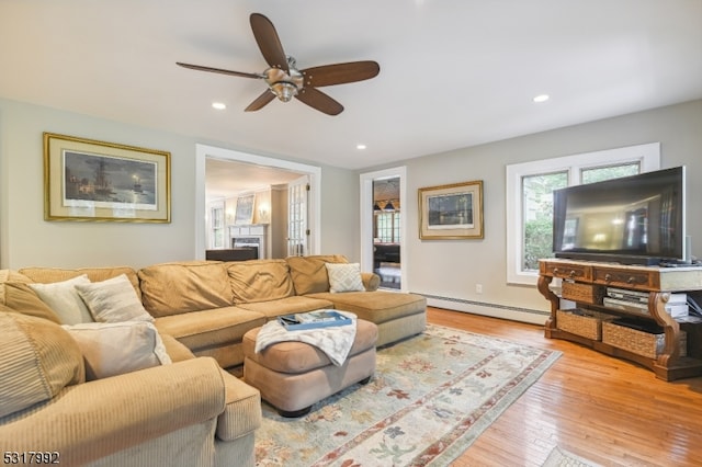 living room with ceiling fan, light hardwood / wood-style flooring, and a baseboard heating unit