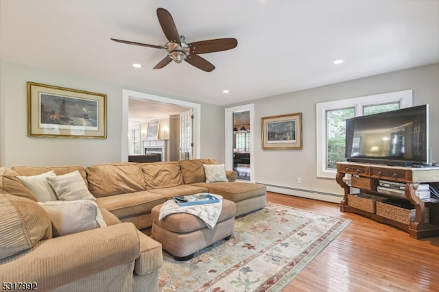 living room featuring light hardwood / wood-style floors, a baseboard heating unit, and ceiling fan