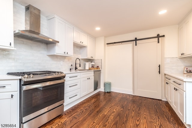 kitchen featuring white cabinets, wall chimney exhaust hood, dark wood-type flooring, stainless steel appliances, and a barn door