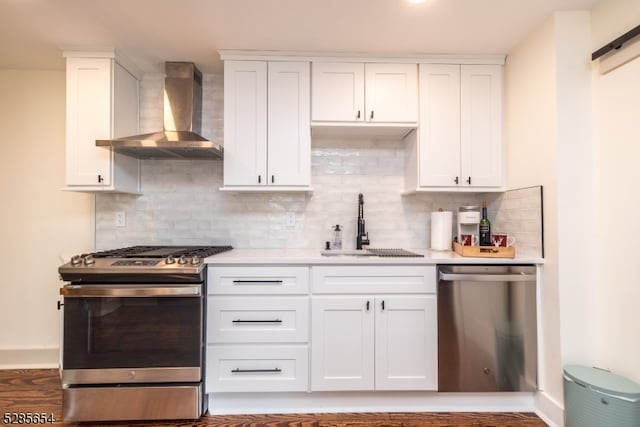 kitchen featuring wall chimney exhaust hood, white cabinetry, stainless steel appliances, a barn door, and dark hardwood / wood-style flooring