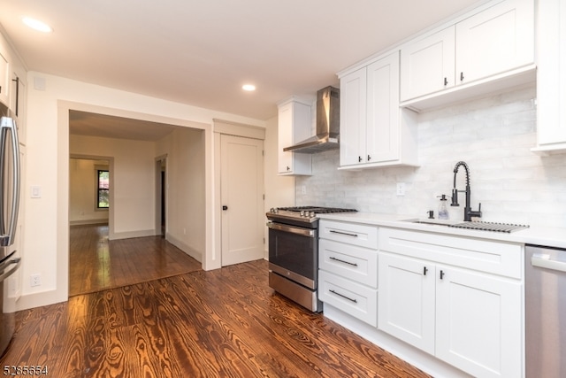 kitchen with dark wood-type flooring, sink, wall chimney range hood, white cabinetry, and appliances with stainless steel finishes