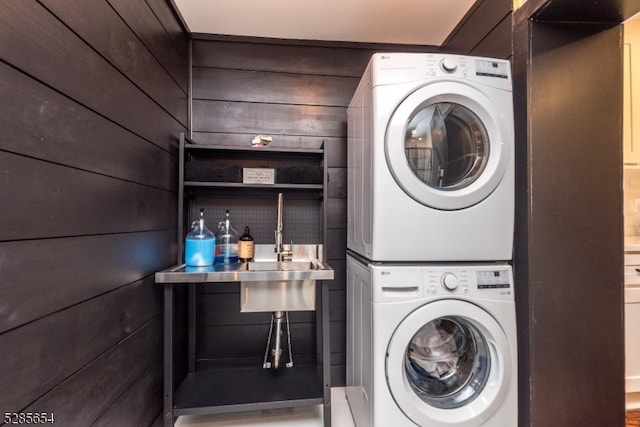 clothes washing area with stacked washer and dryer and wood walls