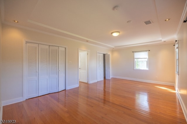 unfurnished bedroom with a raised ceiling, ornamental molding, and light hardwood / wood-style flooring