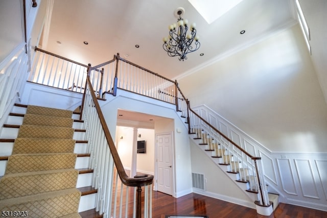 stairway with a skylight, hardwood / wood-style flooring, ornamental molding, and a high ceiling