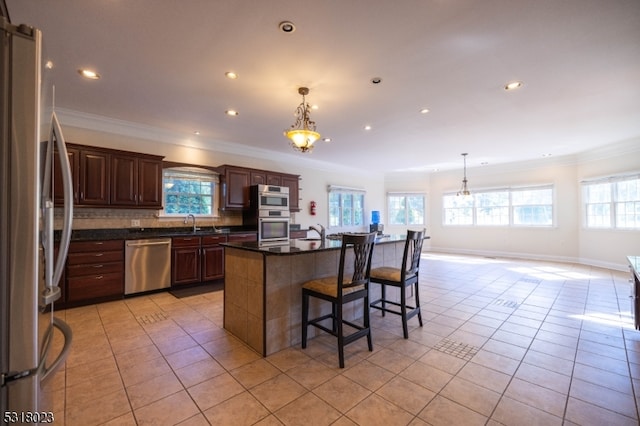 kitchen featuring stainless steel appliances, plenty of natural light, hanging light fixtures, and a kitchen island with sink