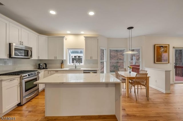 kitchen with pendant lighting, a sink, a center island, stainless steel appliances, and light wood finished floors