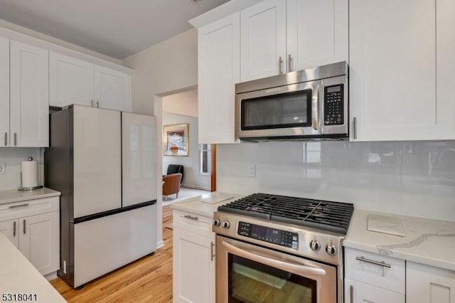 kitchen featuring light wood finished floors, white cabinets, appliances with stainless steel finishes, and light stone counters