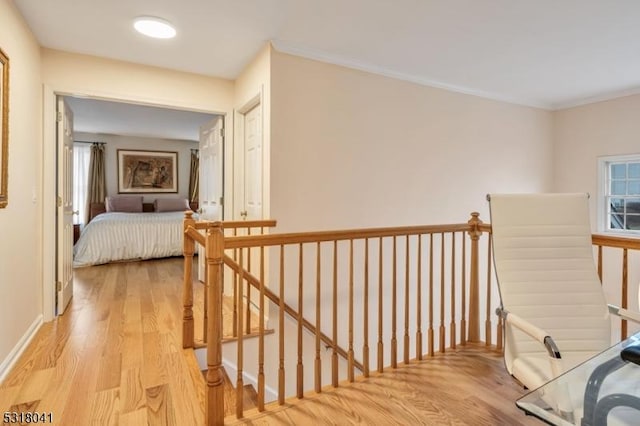 corridor featuring light wood-style flooring, an upstairs landing, baseboards, and ornamental molding