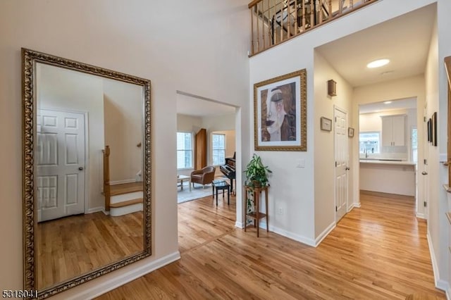 entryway with baseboards, a towering ceiling, and light wood finished floors