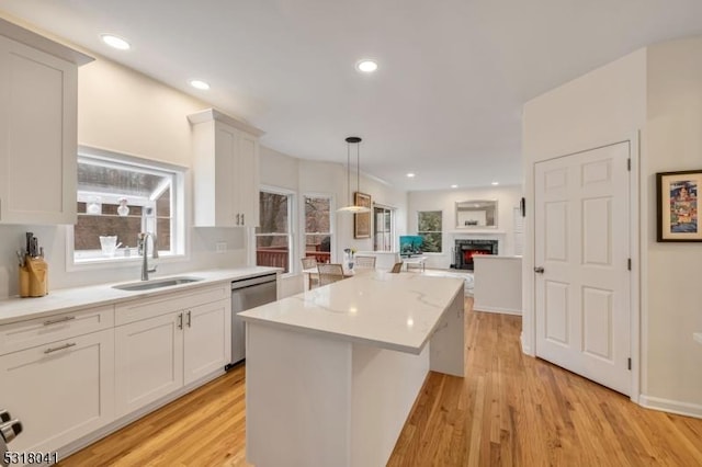 kitchen with a kitchen island, light wood-style flooring, a sink, light countertops, and dishwasher