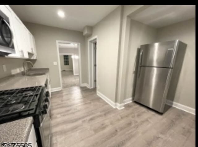 kitchen featuring white cabinets, stainless steel fridge, sink, black gas range, and light hardwood / wood-style flooring