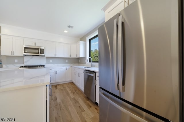 kitchen with appliances with stainless steel finishes, light wood-type flooring, light stone counters, sink, and white cabinetry