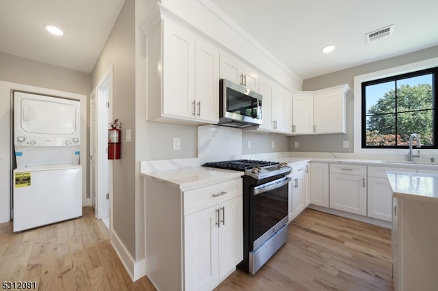 kitchen with stainless steel appliances, sink, stacked washer and clothes dryer, light hardwood / wood-style floors, and white cabinetry