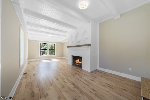 unfurnished living room featuring beamed ceiling, light hardwood / wood-style floors, and a brick fireplace