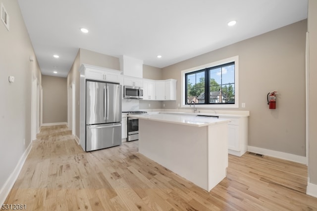 kitchen with white cabinets, a center island, light wood-type flooring, and stainless steel appliances