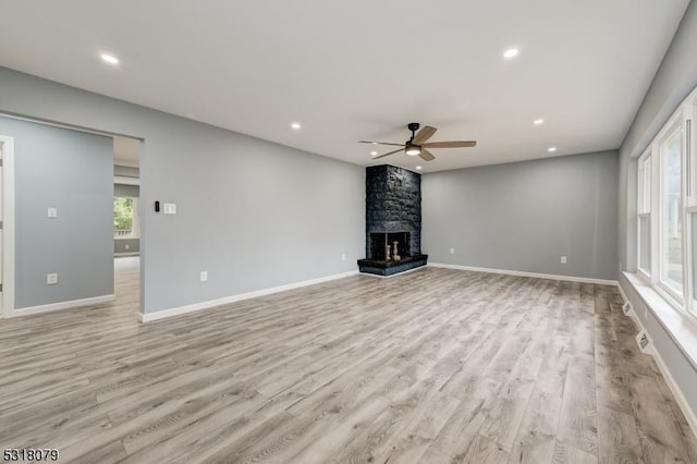 unfurnished living room featuring light wood-type flooring, a large fireplace, and ceiling fan