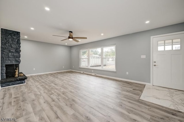 unfurnished living room with light hardwood / wood-style flooring, a stone fireplace, and ceiling fan