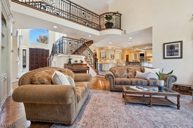 living room with a towering ceiling, ornamental molding, and light wood-type flooring