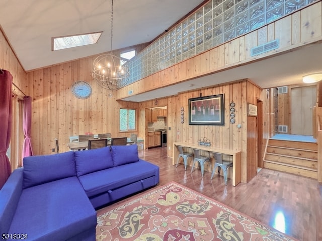 living room with an inviting chandelier, high vaulted ceiling, wood-type flooring, a skylight, and wooden walls