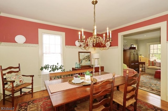 dining space with a wealth of natural light, a notable chandelier, wood finished floors, and ornamental molding