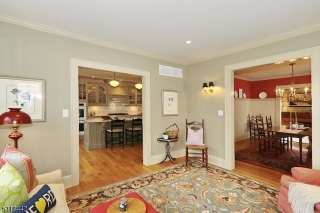 living room featuring crown molding, wood finished floors, visible vents, and a chandelier