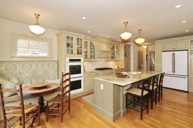 kitchen with light stone counters, a kitchen breakfast bar, tasteful backsplash, white appliances, and light wood finished floors