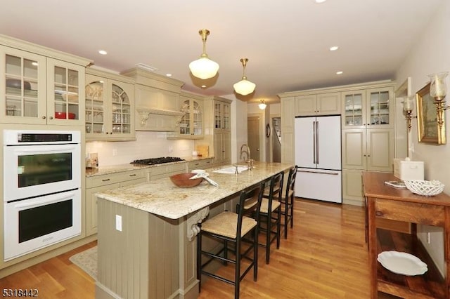 kitchen with a kitchen bar, cream cabinetry, light stone counters, white appliances, and light wood finished floors