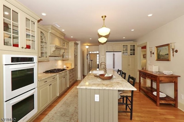 kitchen with a kitchen breakfast bar, cream cabinets, light wood-style floors, white appliances, and a sink