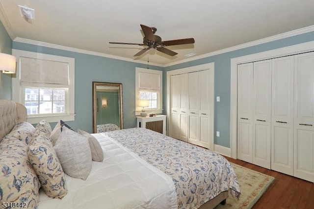 bedroom with dark wood finished floors, two closets, a ceiling fan, and ornamental molding