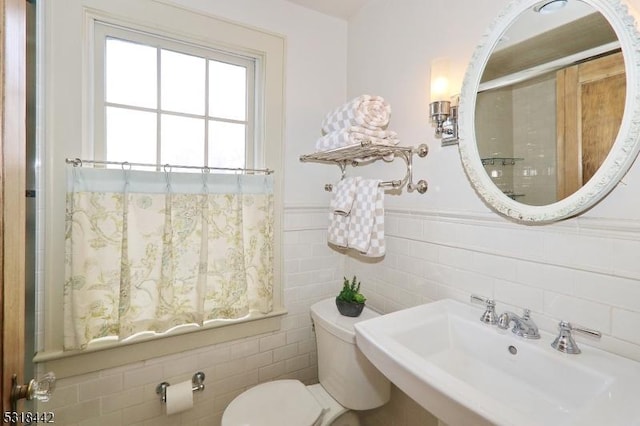 bathroom with tile walls, toilet, a wainscoted wall, and a sink