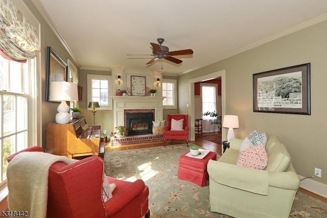 living area with wood finished floors, baseboards, ceiling fan, ornamental molding, and a brick fireplace