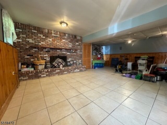 basement featuring tile patterned flooring, brick wall, wood walls, a fireplace, and wainscoting