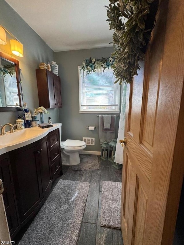 bathroom with baseboards, visible vents, toilet, wood finished floors, and vanity