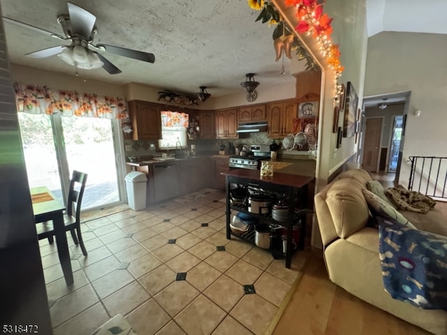 kitchen with lofted ceiling, light tile patterned floors, stainless steel gas range oven, under cabinet range hood, and decorative backsplash